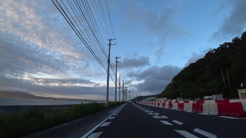 OKINAWA, JAPAN - AUG 2021 : Driving around Nago city area in sunset time. Point of view (POV), seaside road driving shot. Romantic summer holiday, vacation and travel concept.