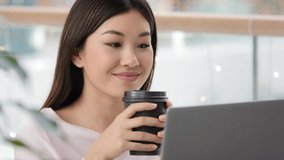 Portrait calm relaxed asian girl user blogger freelancer student woman with laptop watching video online drinking tea coffee cappuccino from paper cup in cafe office business chatting business smiling