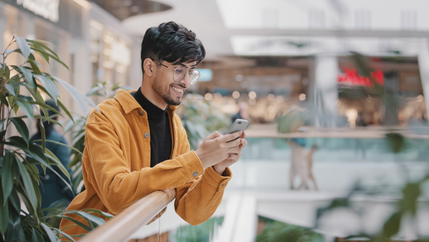 Happy smiling young arab guy stands with telephone in hands typing message on dating site chatting with friends using mobile application on smartphone writes sms checks email browses social networks Royalty-Free Stock Footage #1088336983