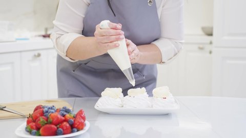 a female chef adds cream from a pastry bag to Anna Pavlova cakes in the kitchen. recipes for delicious traditional desserts. cooking school and courses. Record video and photo lessons.