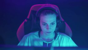 Portrait of an emotional female gamer in headphones, plays a video game, young cyber sportsman shouts and communicates with the team at a tense moment, emotions of victory.