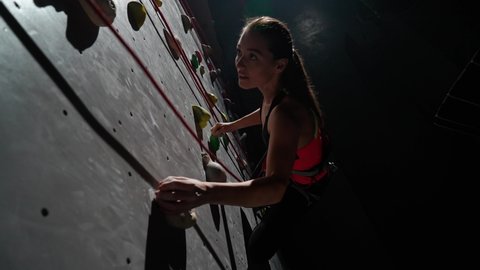 Woman climber training on a climbing wall, practicing rock-climbing and moving up, endurance training, view from the top.