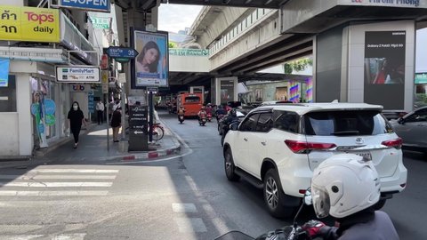 BANGKOK, THAILAND - Circa November, 2021: People walking and cars passing at Soi Sukhumvit 35, Phrom Phong BTS Station near The Emporium shopping mall on a sunny day. Family mart on street corner
