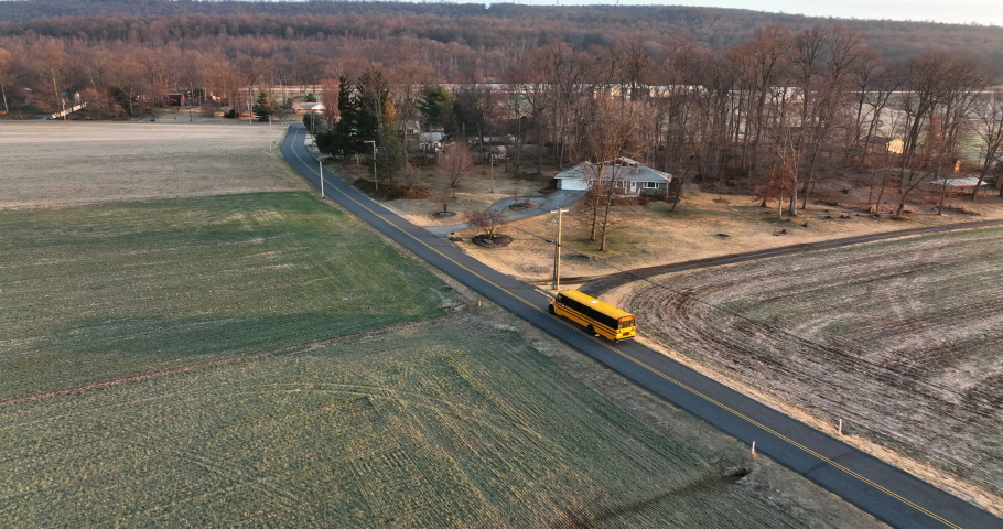 School bus drives on road through rural American countryside. Homes at winter sunrise. Aerial view. Royalty-Free Stock Footage #1088341331