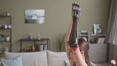 Slowmo shot of concentrated young Caucasian woman with high-tech prosthetic arm practicing yoga at home