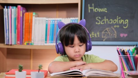 Cute little girl with headphones listening to audiobooks and looking at English learning books on the table. Learning English and modern education
