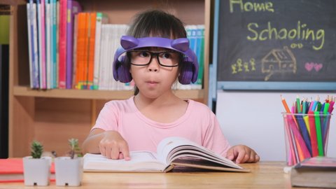 Cute little girl with headphones listening to audiobooks and looking at books at home. Learning English and modern education