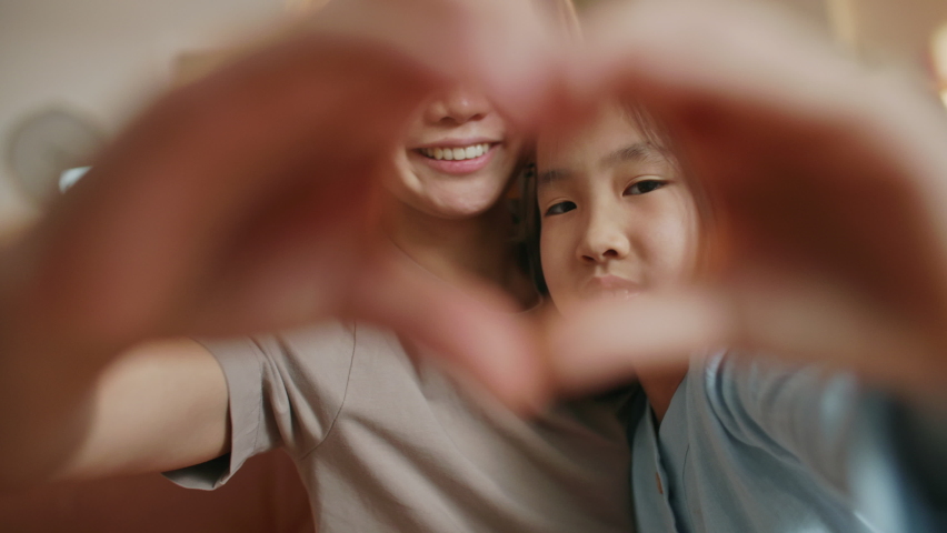 Beautiful Asian Happy Mother and Little Cute Daughter Faces Seen Through Joined Fingers Making Heart Shape, Close Up. Symbol of Love, Cherish, Family Bonding, Donation Sign, Adoption and Custody Royalty-Free Stock Footage #1088345103