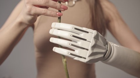 Slowmo closeup portrait of young beautiful Caucasian woman with high-tech prosthetic arm holding flower on thin stem
