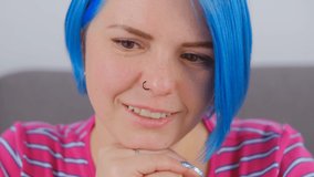 Cute Ukrainian woman with blue hair reading from computer screen. Portrait of stylish white female with nose piercing and dyed bob hairstyle looking in laptop monitor with cheerful smile