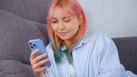Cute white girl browsing social media news feed in mobile phone and laughing. Pretty young Ukrainian woman with dyed rainbow hair using modern smartphone for online entertainment 