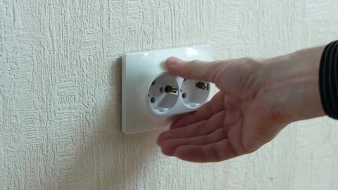 Faulty, weakened electrical outlet sticking out of the wall in the apartment. Repair of a faulty electrical outlet. A man touches a socket protruding from the wall
