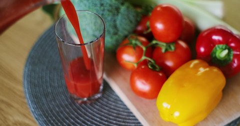 Woman pouring fresh tomato juice in glass on fresh vegetables background.
