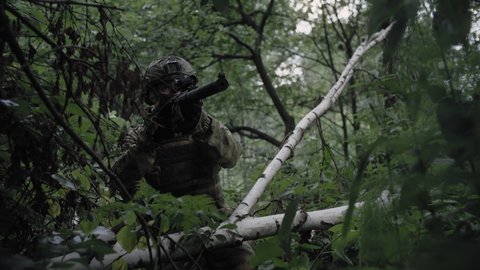 Close-up, an armed soldier with a sniper rifle, in a dense forest, protects the front line, on alert. Equipped soldier in action