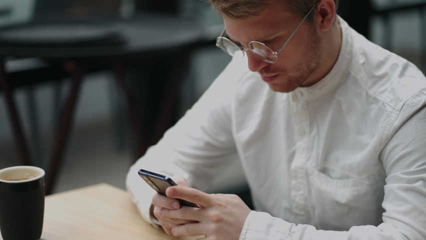 Adult businessman texting on smartphone while sitting by laptop
