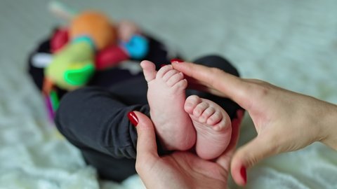 Mother is taking her child's feet in hands. Little baby moving tiny toes to avoid tickles. Blurred backdrop.