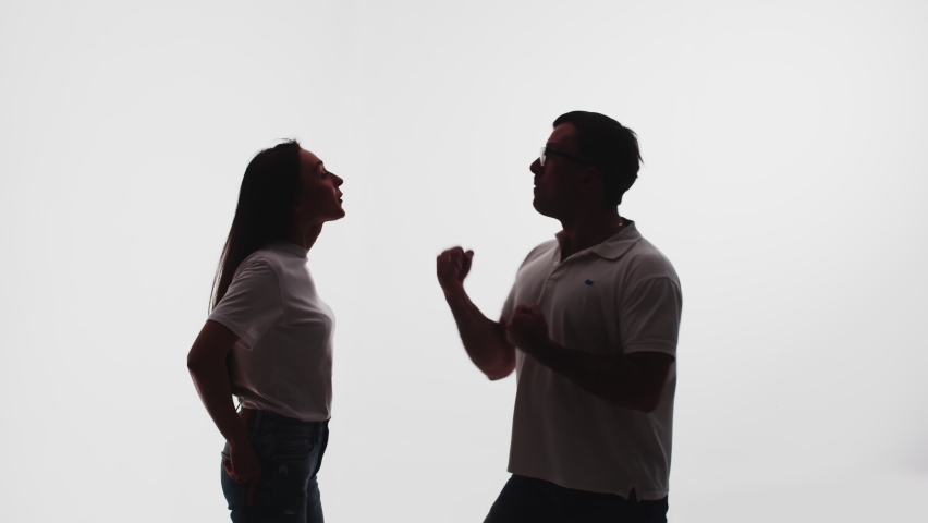 Silhouette of man who threatens woman that will hit her, she stands confidently and is not afraid of him, white background in studio, side view. Concept confidence and bravery Royalty-Free Stock Footage #1088351405