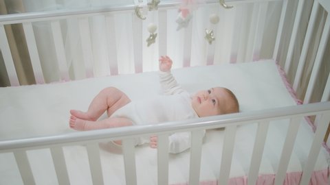 Charismatic pretty baby girl playing with her cot toys while laying down in her baby cot concept of childhood and maternity