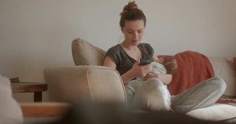 Mum breastfeeding her newborn baby and using a smartphone