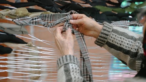 Ukraine, Chernivtsi- March 4, 2022:Grandmother weaves camouflage net from fabric for Ukrainian troops defending territory of Ukraine during war. Protective net helps to hide from enemies. Volunteering