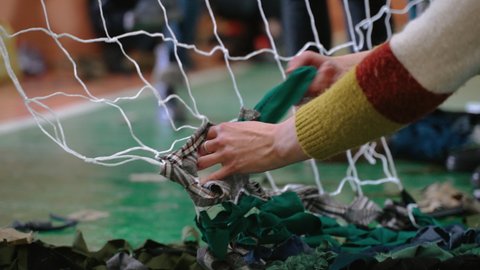 Weaving camouflage net from ribbons of fabric for Ukrainian troops defending territory of Ukraine during war. Protective net helps to hide from enemies. Volunteering. Assistance to Ukrainian defenders