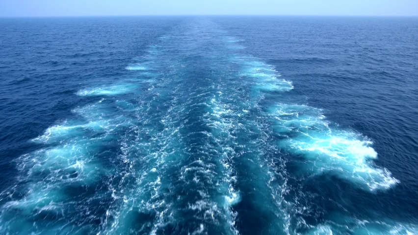 Wake of vessel. Wide wake trail from boat. Back view. Ocean water. Deep blue. Trace from large ship.