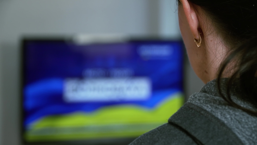 Unrecognizable woman watches news on TV about military conflict between Russia and Ukraine. Crisis, peace, stop aggression in whole world