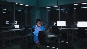 African-American businessman having video call on laptop overworking at night. Young executive talk on video chat with team working late in dark office