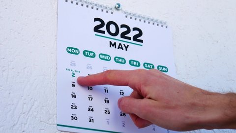 Close-up of male hands tearing off the wall calendar April page 2022 and pointing finger to Eid al-Fitr date on the next one