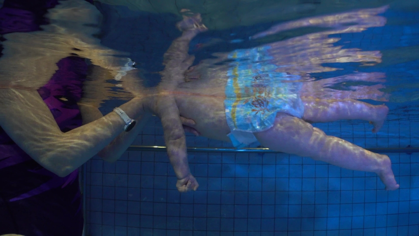 Little baby and her mother having swimming lesson in the pool. Mother is holding her daughter in her hands. Underwater shot.
