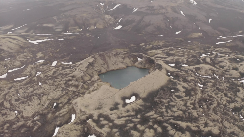 Descending aerial drone shot of Tjarnagigur Crater Lake in Lakagigar Region Iceland during snowfall