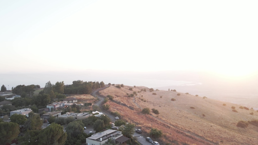 Aerial view overlooking houses and a road in the highlands of Golan Heights, sunset in Israel - ascending, tilt, drone shot
