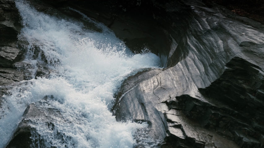 The torrent of the whitewater rushes over the rocks. Close-up, slow-motion.