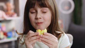 Attractive brunette school girl on a home background, licks her lips, eating one yellow macaron, closes her eyes with pleasure. Dessert person, sweet tooth, gourmet. Feeling good, delicious - Powered by Shutterstock - Get 15% off with code: PIKWIZARD15