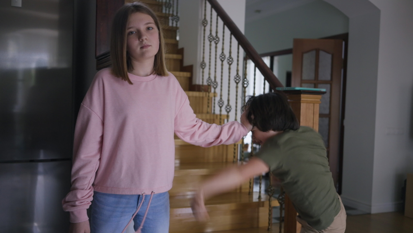 Portrait of Caucasian teenage girl ignoring little boy fighting with sibling. Indifferent sister looking at camera holding brother head as child moving hands trying reach teenager Royalty-Free Stock Footage #1088363121