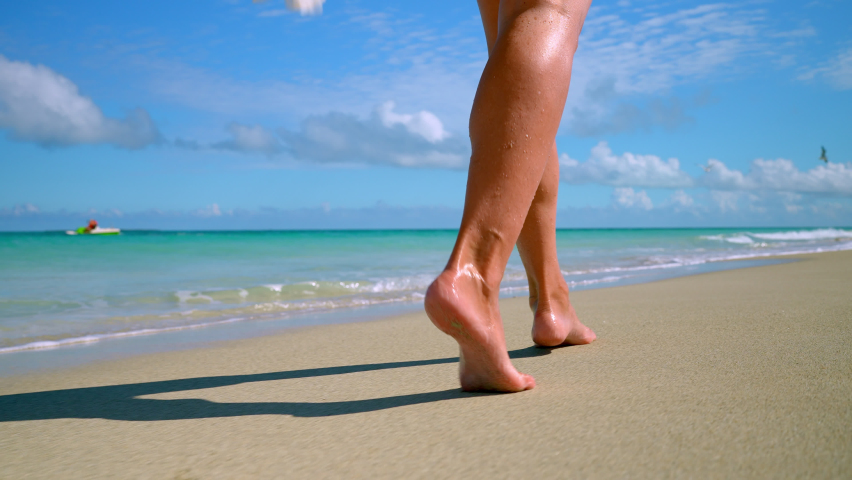 women's feet walk along the sandy beach to the shore of the blue sea. Royalty-Free Stock Footage #1088365245