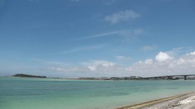 TOMIGUSUKU, OKINAWA, JAPAN - AUGUST 2021 : View of Senaga island and beach (Ocean or sea) in daytime. Clear blue summer sky and clouds. Holiday, vacation and resort concept video. Time lapse shot.