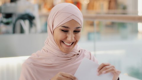 Close-up young excited happy arab woman in hijab receiving letter reading good incredible news smiling excellent medical test result approve for new job pay raise celebrates success feeling euphoric