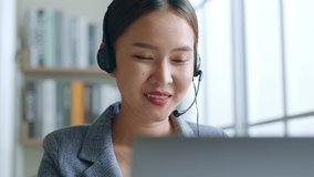 Close up of Young Asian businesswoman wearing headphone, call center, customer service talking on video call conference or virtual meeting in office, front view
