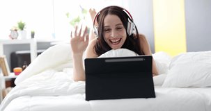 Smiling woman in headphones communicates by video call while lying in bed