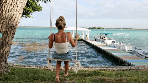 Slow motion: Woman on a swing contemplating beautiful lake 