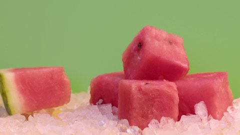 A slice of watermelon in cold ice on a green background, ice falls on the watermelon slowly from the top. Slow motion footage, 8K downscale,  filmed on high speed cinema camera. 4K.