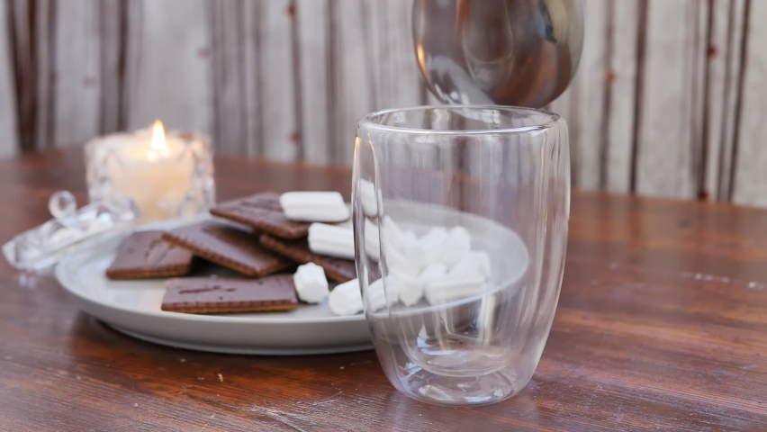 A woman's hand pours milk hot cocoa into a glass glass and adds marshmallow. Delicious drink with chocolate and vanilla aroma. slow motion Royalty-Free Stock Footage #1088376833