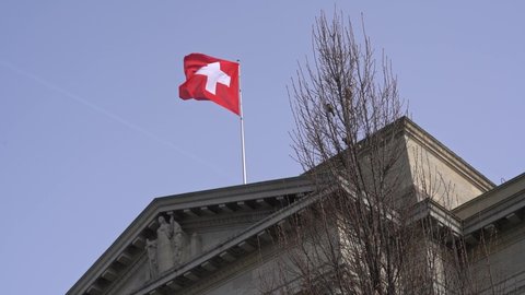 Flag of Switzerland waving on top of Federal Supreme Court building at City of Lausanne, Canton Vaud, on a blue and cloudy spring day. Slow motion movie shot March 18th, 2022, Lausanne, Switzerland.