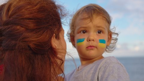 Close up portrait little baby and mom with flag of Ukraine on face. Protest against Russian war invasion in Ukraine. Ukrainian Flag, Protesters concept