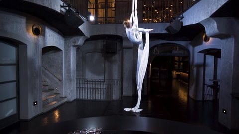 Female aerialist doing a front split pose on silks with her knees bent.