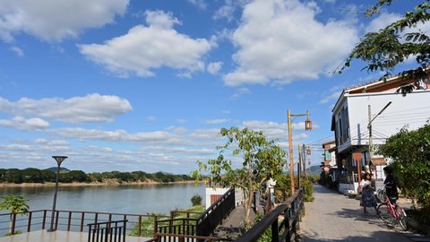 Chiang Khan , Loei , Thailand - 01 01 2022: Some people taking turns in taking pictures while the sky is blue and clouds are moving captured in a time lapse, Walking Street, Chiang Khan, Loei in Thail
