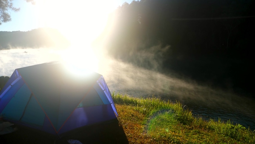 Camping tent near mist river in nature background with bright sunrise scenic view at lake and forest pine tree. Fog lake on early morning dusk. Beautiful landscape. Relax on nature. Bright sunshine