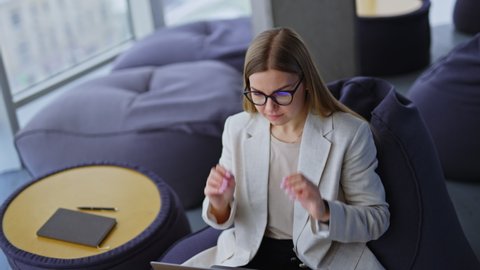 Pleasant-looking woman in glasses leans back and sits comfortably in bean bag chair with laptop on her legs. Modern office work concept.