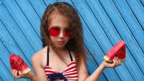 A curly-haired brunette girl enjoys eating a juicy piece of red watermelon. The child's hair develops in the wind. A child in a swimsuit eats refreshing food on a hot sunny day - Powered by Shutterstock - Get 15% off with code: PIKWIZARD15